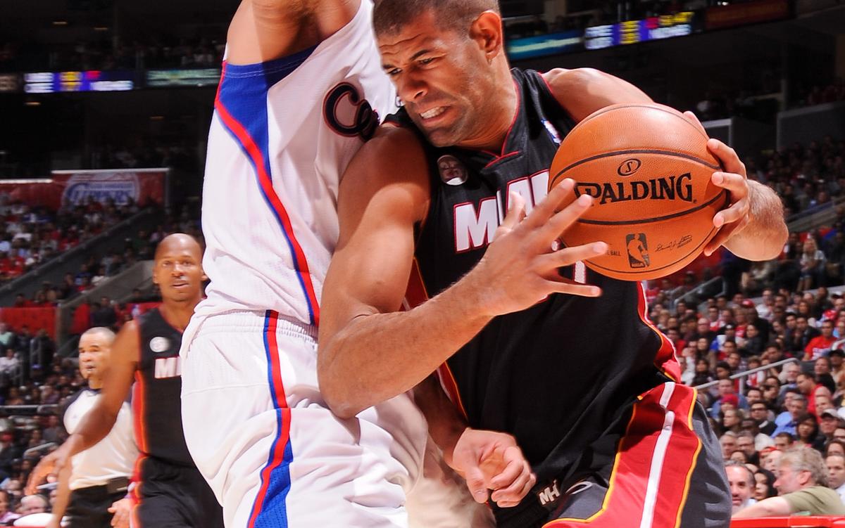 Two basketball players in action, one holding running past the other while holding the ball, with a crowd and referee in the background.